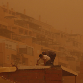 Unas personas trabajan en Aguadulce, Roquetas de Mar (Almería), que ha amanecido este martes bajo los efectos de una intensa calima.
