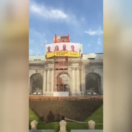 La Puerta de Alcalá amanece tapada por una pancarta con la cara de los candidatos y la frase: "¿El cambio climático os la suda?"