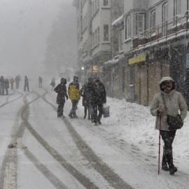 Turistas y habitantes de Canfranc caminan por una calle cubierta de nieve. La nieve caída en las últimas horas en el Pirineo de Huesca mantiene cortadas al tráfico dos carreteras y en otras 25 es necesario el uso de cadenas o neumáticos de 