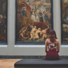 Mujer sentada en un banco delante de tres pinturas. Fuente: Pexels