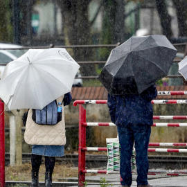 Viandantes esperan un paso a nivel bajo una intensa lluvia, a 2 de marzo de 2025, en Avilés.