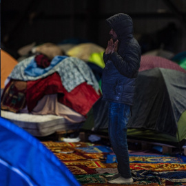 Un migrante reza en un almacén abandonado, donde se ha formado un campamento improvisado para refugiarse durante los meses de invierno, en Marck, cerca de Calais, en el norte de Francia.
