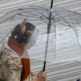 Imagen de una fallera protegiéndose de la lluvia, a 18 de marzo de 2025, en València.