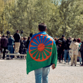 Una persona con una bandera gitana a su espalda durante el acto conmemorativo del Día Internacional del Pueblo Gitano, en los jardines bajos del puente de Segovia, a 13 de abril de 2023, en Madrid (España)
