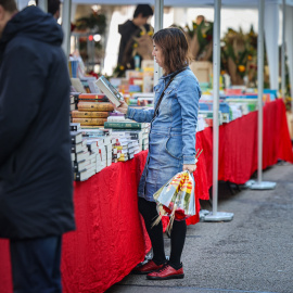 Una noia amb una rosa fulleja un llibre en una parada del centre de Barcelona per Sant Jordi