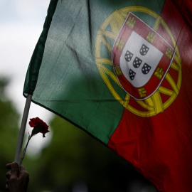 Una mujer sostiene un clavel rojo y la bandera portuguesa durante la manifestación del 25 de abril en la Avenida da Liberdade de Lisboa, a 25 de abril de 2024.