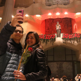 Una parella fent-se una foto al davant del Sant Jordi de la Sagrada Família amb la rosa i el llibre que els han donat abans de la visita guiada