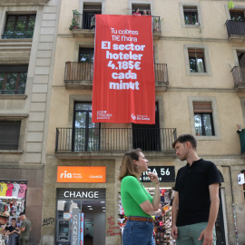 La presidenta del grup municipal de BComú, Janet Sanz, i el portaveu de la formació, Max Cahner, observen la pancarta de grans dimensions que el partit ha penjat en el marc de la campanya contra el turisme massiu