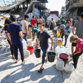 Niños palestinos llevan bidones llenos de agua distribuida por un camión cisterna.