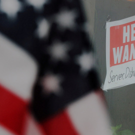 Un letrero ofrece empleo en la ventana de un restaurante  en la localidad de Medford (Massachusetts), con el reflejo de una bandera estadounidense ondeando.