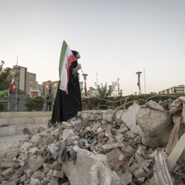 Una estudiante iraní sujeta la bandera de Irán encima de los restos de un edificio destruido en Tehran el 21 de junio de 2025.