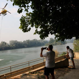 La gente observa cómo un helicóptero vuela para ayudar a extinguir un incendio forestal en Tarragona, a 8 de julio de 2025.