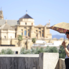 Una mujer se tapa con una sombrilla mientras camina por el Puente Romano, en Córdoba.