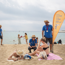 Dos informadores conversan de la nueva prohibición de fumar con bañistas, en la playa del Bogatell (Barcelona).