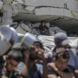 Gaza City (-), 04/08/2025.- A boy (rear) sitting among the rubble of a damaged building looks on as internally displaced Palestinians gather to receive food from a charity kitchen, in Gaza City, Gaza Strip, 04 August 2025. Humanitarian organizations have warned of an imminent food catastrophe for thousands of children, a crisis caused by severe food insecurity, a decline in health services, and ongoing restrictions on humanitarian aid and essential supplies. EFE/EPA/MOHAMMED SABER