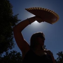Una mujer se protege con un abanico del sol.