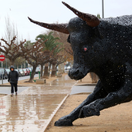 Una persona pasa junto a la figura del toro que hace un homenaje a la afición taurina de Amposta.