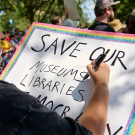 Un mujer escribe una pancarta abogando por la preservación de museos y bibliotecas durante una marcha por Washington D.C. en protesta por el despliegue de la Guardia Nacional decretada por Donald Trump.