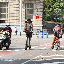 Una moto, un patinet i una bici circulen per un carrer de Barcelona