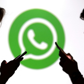 Unos jóvenes con sus smartphones en frente del logo de la aplicación Whatsapp.