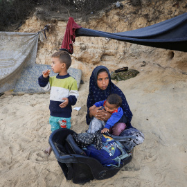 Palestinos desplazados, que huyeron del norte de Gaza, descansan junto a sus pertenencias al borde de una carretera en el centro de la Franja.