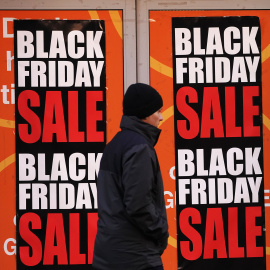 Foto de archivo de un hombre junto a los carteles de ofertas del Black Friday.