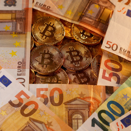 Billetes de euro junto a monedas que representan el bitcoin, la criptomoneda más popular.