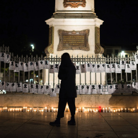 Una mujer pasa junto a velas encendidas y pancartas en la Plaza de la Merced de Málaga, con motivo del Día Internacional para la Eliminación de la Violencia contra las Mujeres en 2021.