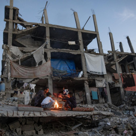 Palestinos desplazados se calientan junto a una fogata entre las ruinas de su hogar destruido en Khan Yunis, sur de la Franja de Gaza, el 30 de diciembre de 2025.