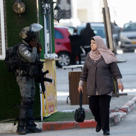 Una mujer palestina camina junto a un miembro de las fuerzas israelíes, en la Cisjordania ocupada por Israel.