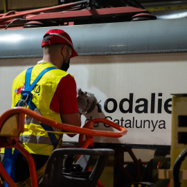 Un treballador neteja el logotip de Rodalies en un tren estacionat a una base de manteniment