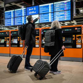 Dos usuaris miren les pantalles de l'estació de Sants amb els horaris dels trens.