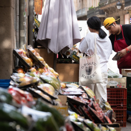 Trabajador de una frutería atendiendo a una clienta, en Barcelona.
