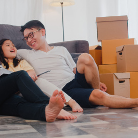 happy-asian-young-family-homeowners-bought-new-house-chinese-mom-dad-daughter-embracing-looking-forward-future-new-home-after-moving-relocation-sitting-floor-with-boxes-together