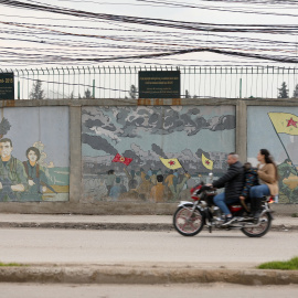 Una motocicleta pasa junto a unos murales de combatientes kurdos en Qamishli (Siria).