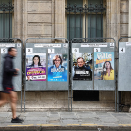 Un hombre corre junto a carteles de campaña electoral con los candidatos a la alcaldía de París.