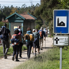 Un grupo de peregrinos pasa frente a un cartel que indica el horario de misas mientras realizan el Camino de Santiago.