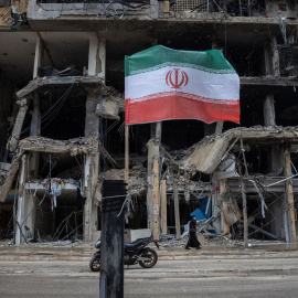 Una bandera iraní ondea mientras una mujer camina junto a un edificio destruido tras los ataques de Israel en los suburbios del sur de Beirut, Líbano.