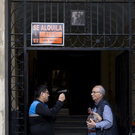 Imagen de archivo de dos hombres charlando bajo un cartel de 'se alquila' en un portal de Madrid.