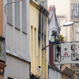 Un bombero procede al desalojo de un vecino del edificio donde ha explotado una bombona de butano en la calle Venero de Barcelona.