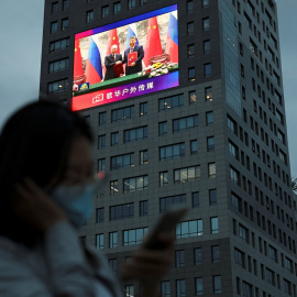 Una mujer cerca de una pantalla gigante que muestra imágenes del encuentro entre el presidente chino Xi Jinping y su homólogo ruso Vladimir Putin.