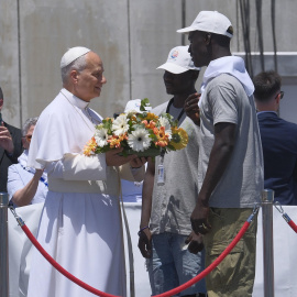 El papa León XIV recibe flores de dos voluntarios para protagonizar una ofrenda floral en el mar en recuerdo de los migrantes muertos en la travesía en el muelle de Arguineguín, en la isla de Gran Canaria,