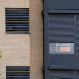 Un edificio con un cartel de 'Se Alquila' bajo la persiana de uno de los pisos.