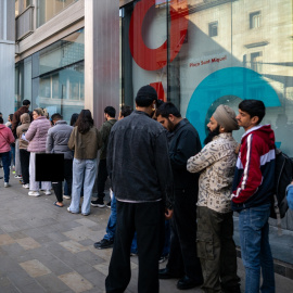 Varias personas migrantes hacen cola en una oficina para presentar los documentos para su regularización.