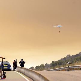 Varias personas observan un helicóptero de extinción sobre el incendio de la Vai d'Uxió en Castelló.
