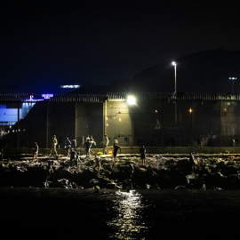 Personas llegan a la orilla del Tarajal tras cruzar a nado la frontera marítima.