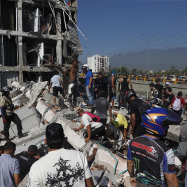 Personas caminan sobre los escombros de un edificio colapsado en Cali (Colombia).
