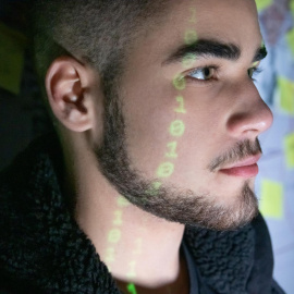 Un joven frente a una proyección de código binario sobre su rostro.