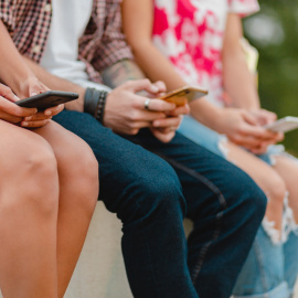 Un grupo de niños y adolescentes utilizan sus móviles sentados en la calle.