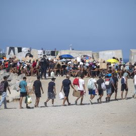 Decenas de migrantes caminan por la playa del Trampolín, a 31 de agosto de 2026.